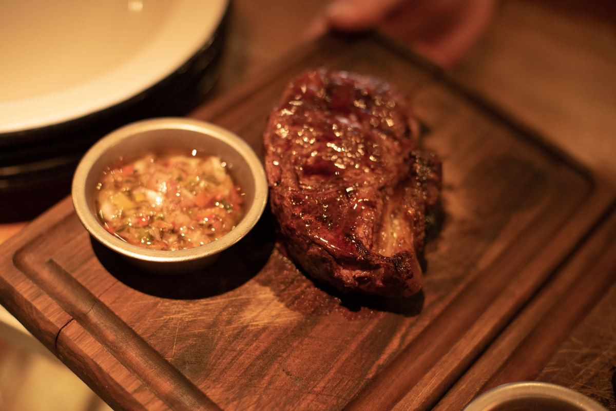 Corte de carne a la parrilla servido sobre tabla con chimichurri