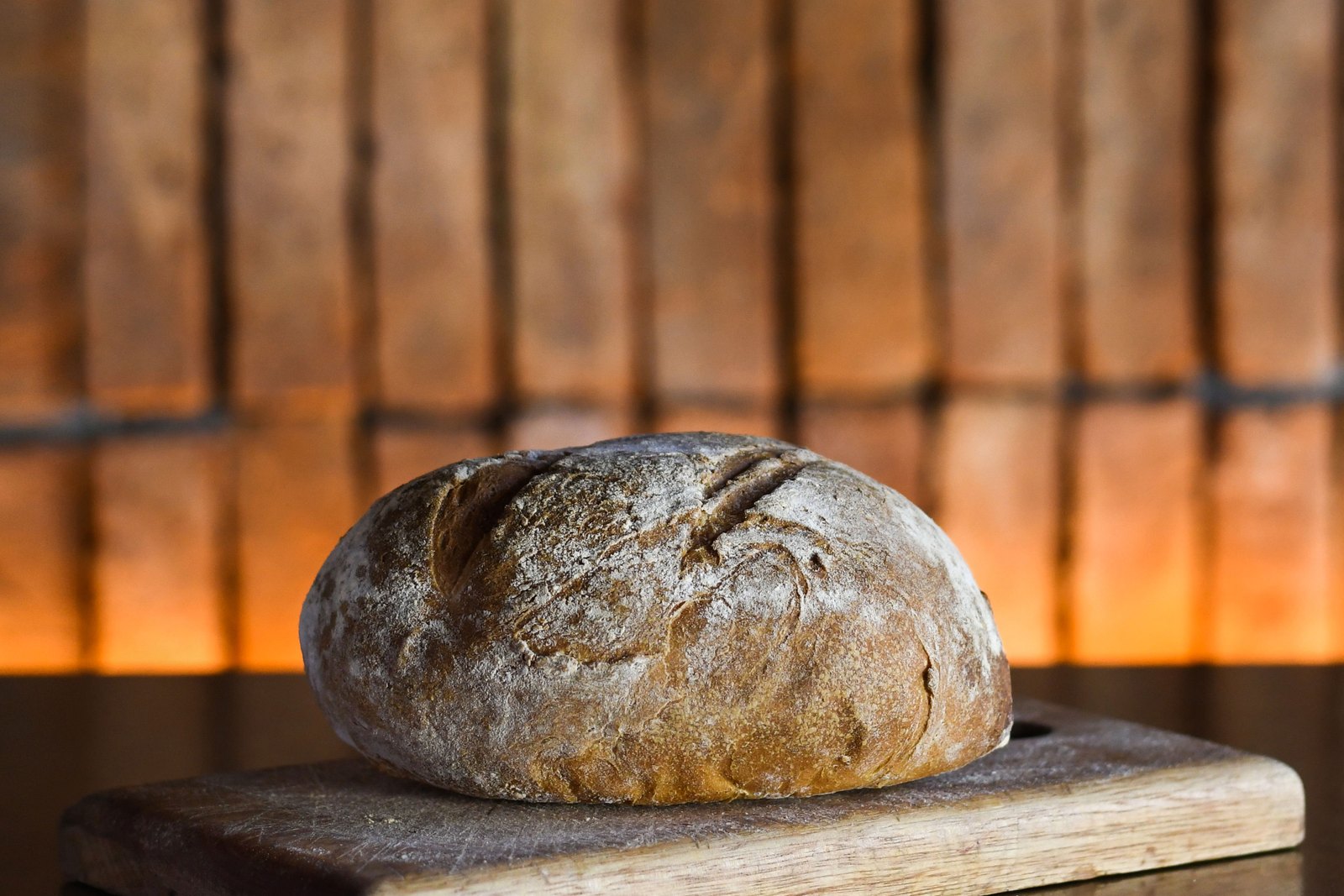 La hogaza de pan casero de Churrasquería sobre una tabla de madera, con las brasas del horno encendidas detrás